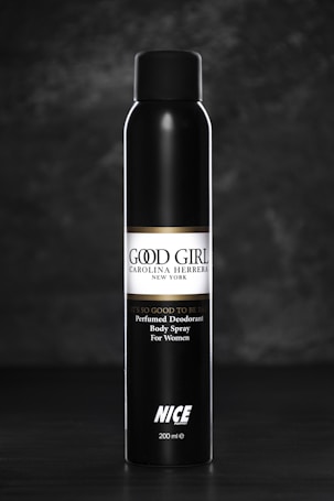 A sleek black bottle of perfumed deodorant body spray for women, labeled 'Good Girl' by Carolina Herrera, with the text 'It's so good to be bad' above the brand name. The bottle stands upright against a dark, textured background.