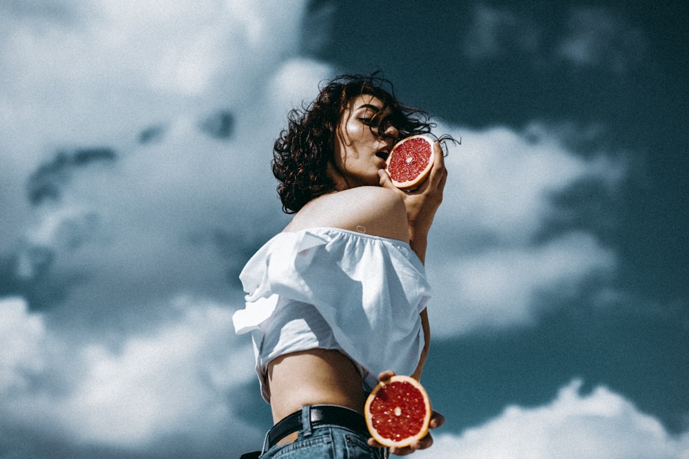 a woman holding two grapefruits up to her face