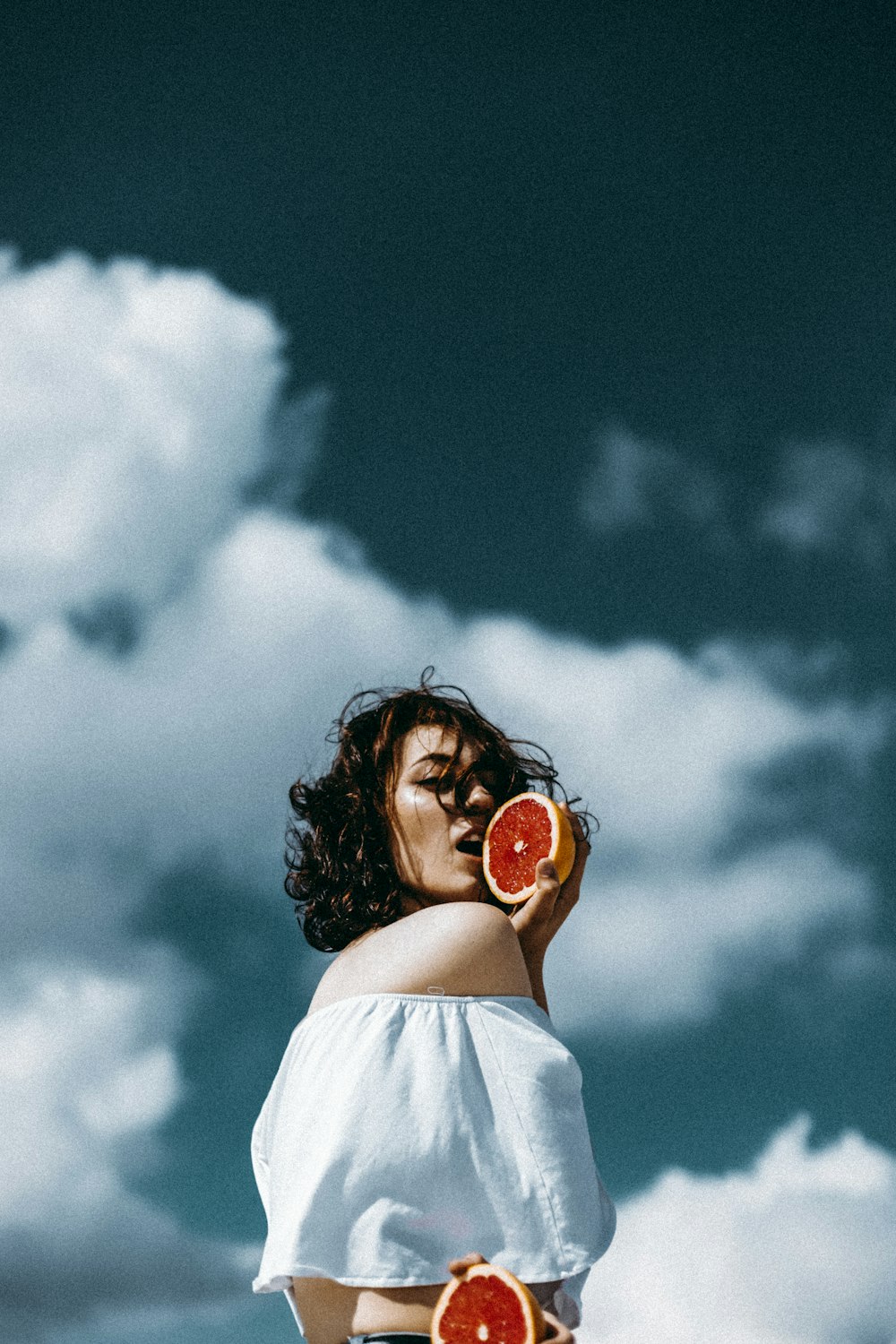 a woman holding two slices of grapefruit in front of her face