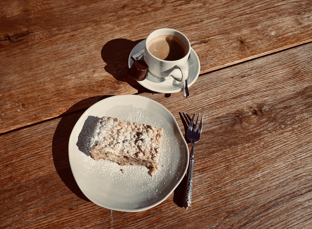 a piece of cake on a plate next to a cup of coffee