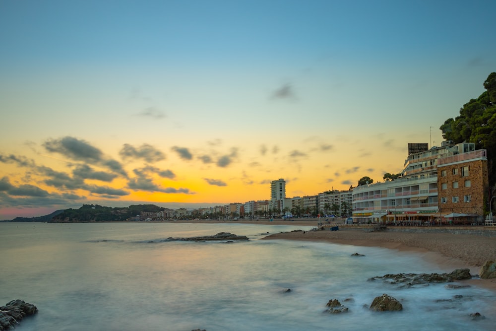 the sun is setting over the beach and buildings