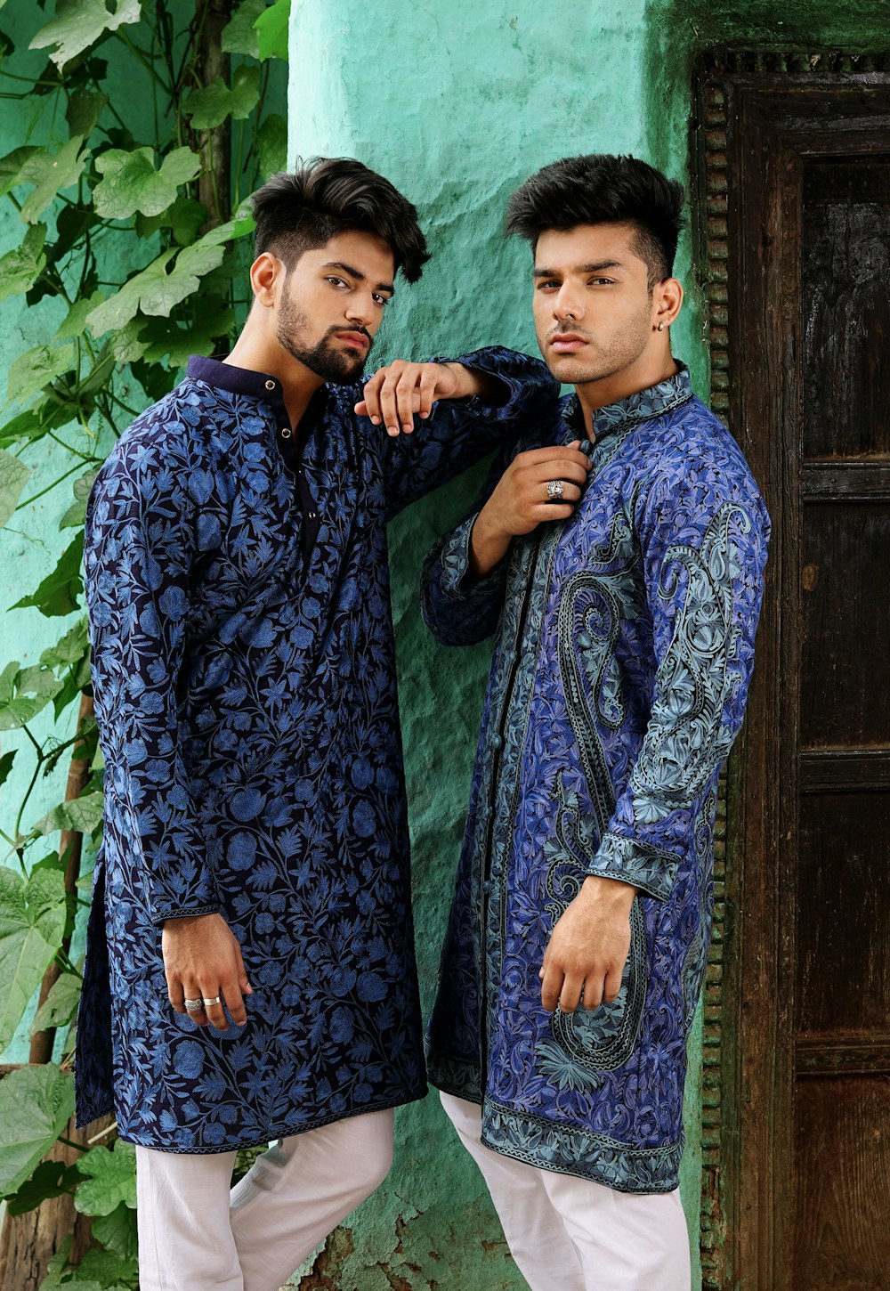 two men standing next to each other in front of a green wall