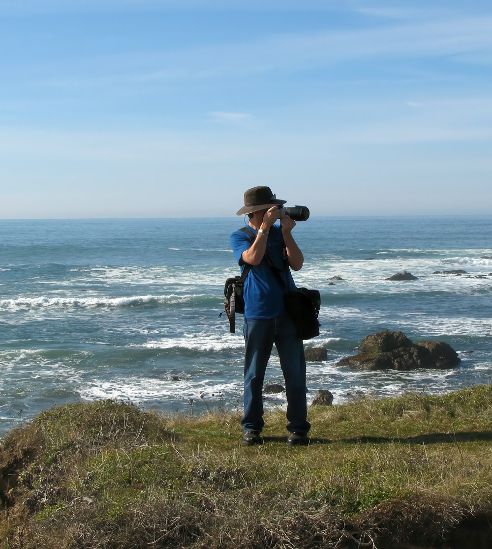 a man standing on top of a lush green hillside next to the ocean