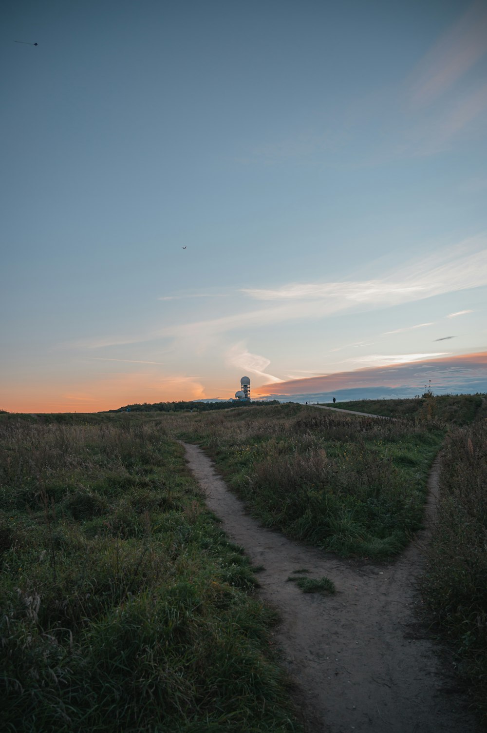 a dirt path in a grassy field with a lighthouse in the distance
