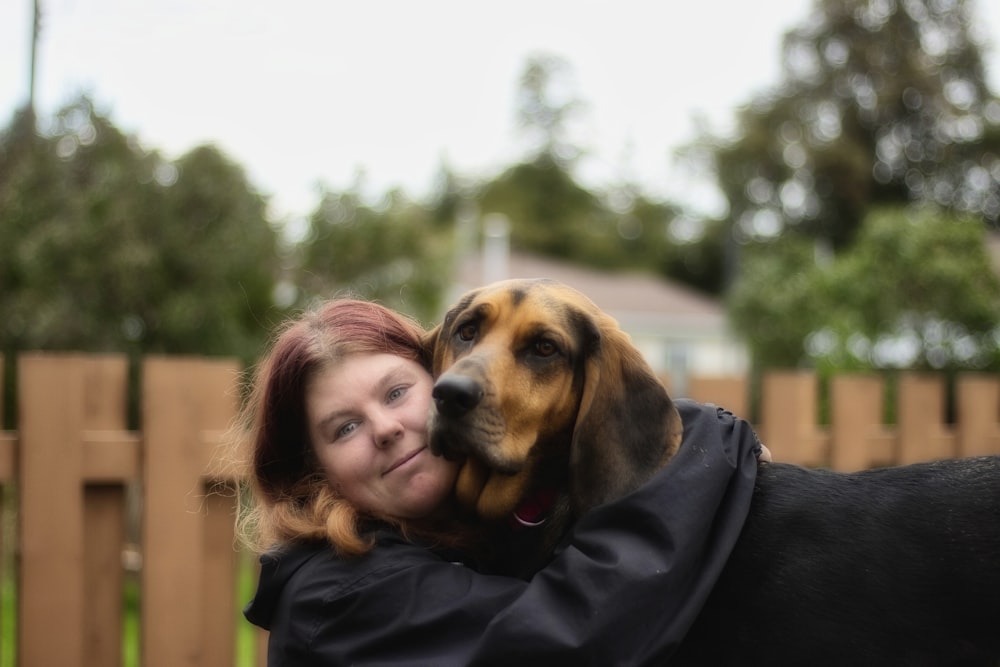 a woman hugging a dog in a fenced in area