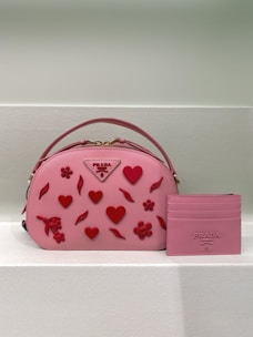 A soft pink heart-shaped bag with delicate stitching, placed on a floral fabric background.