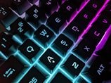 A close-up of a mechanical keyboard with colorful backlighting glowing in a dim room.