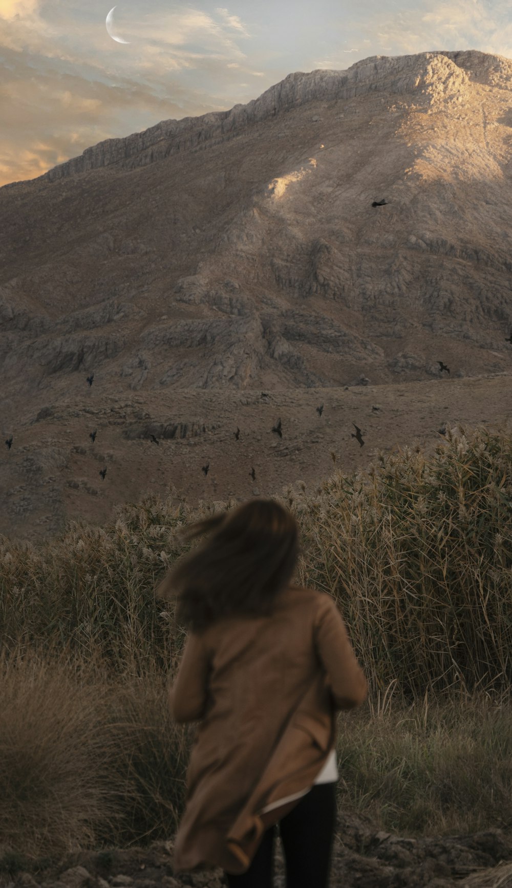 a woman walking down a dirt road next to a mountain