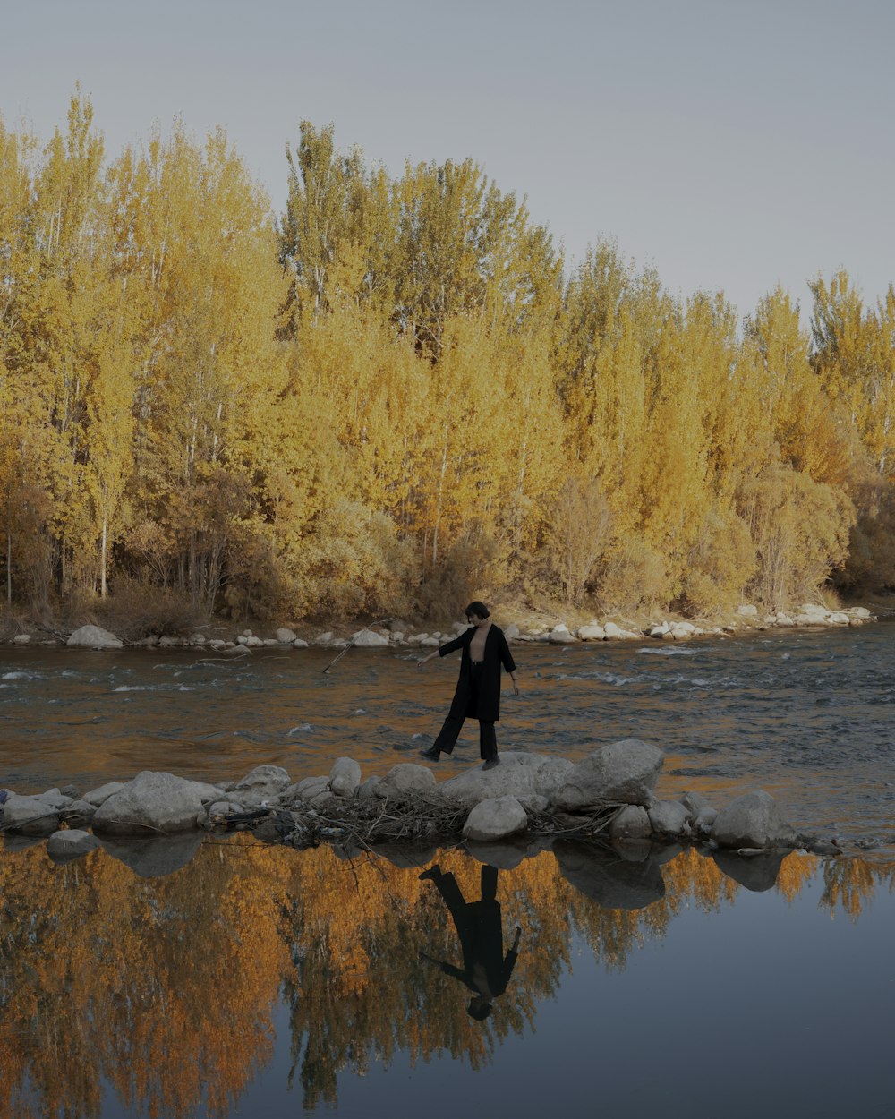 a man walking across a river next to a forest