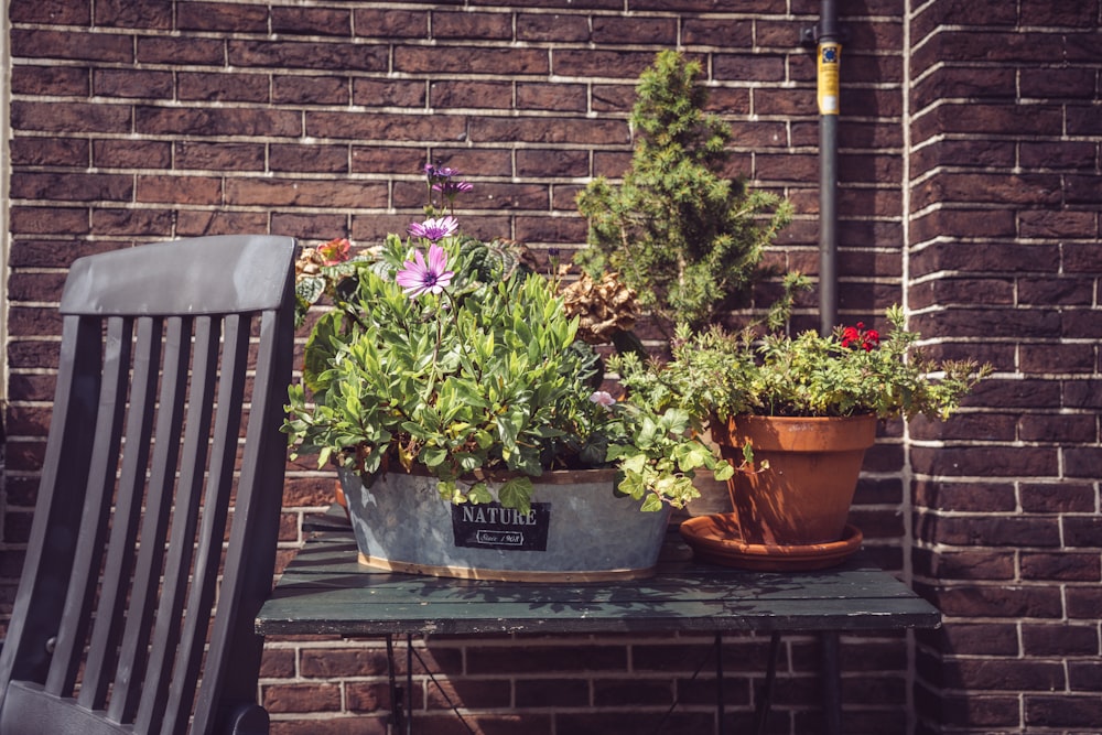 a wooden table topped with potted plants next to a brick wall