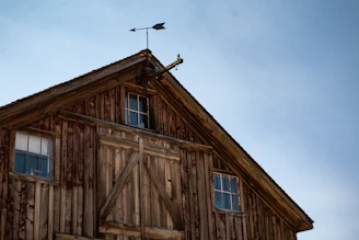 A handcrafted wooden cupola atop a barn roof against a clear blue sky.