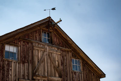 A handcrafted wooden cupola atop a barn roof against a clear blue sky.