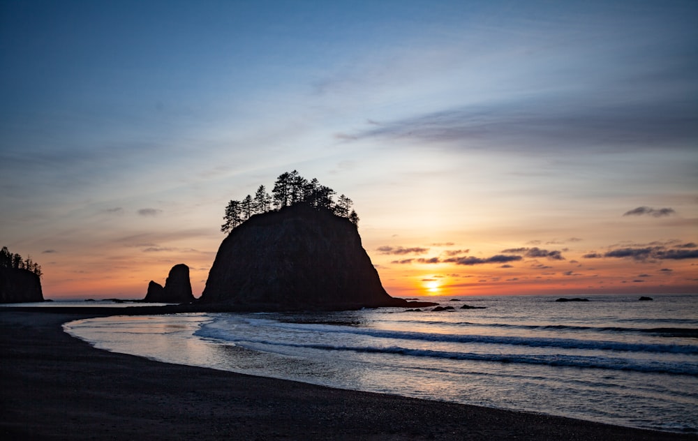 the sun is setting over the ocean with a rock formation in the foreground