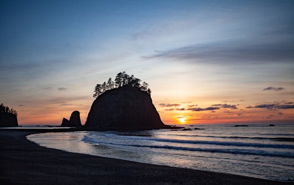 Le soleil se couche sur l’océan avec une formation rocheuse au premier plan