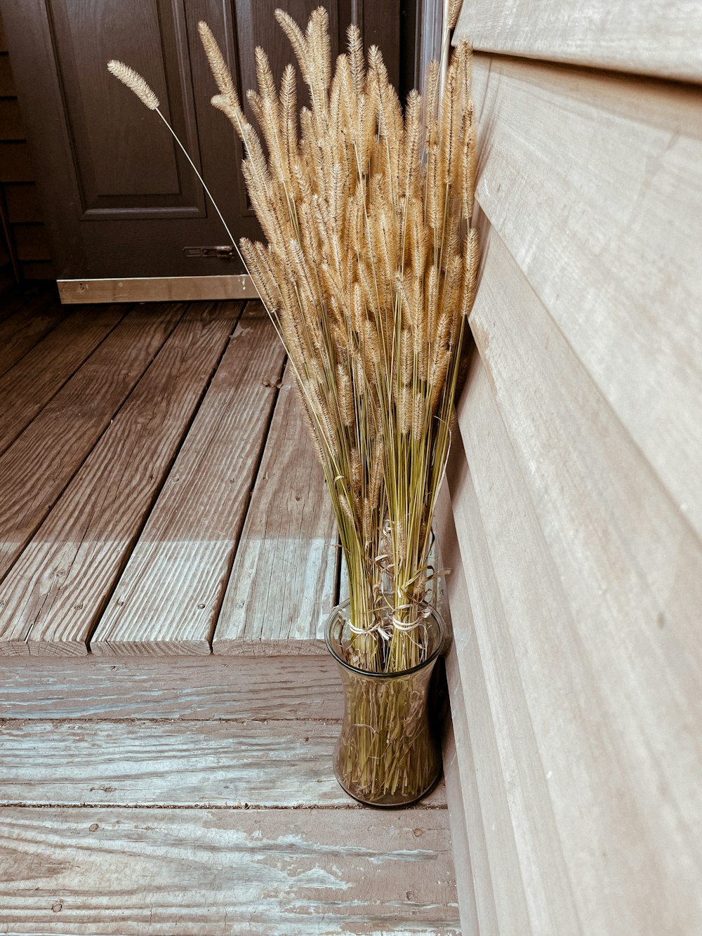 a vase filled with dry grass sitting on top of a wooden floor