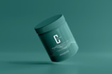 A green cosmetic jar with a minimalist design, featuring the letter 'C' prominently on its front. The jar appears to be floating against a solid green background, creating a sense of simplicity and elegance.