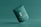 A green cosmetic jar with a minimalist design, featuring the letter 'C' prominently on its front. The jar appears to be floating against a solid green background, creating a sense of simplicity and elegance.