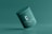 A green cosmetic jar with a minimalist design, featuring the letter 'C' prominently on its front. The jar appears to be floating against a solid green background, creating a sense of simplicity and elegance.