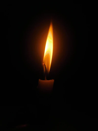 A softly glowing candle flame flickering in the dark, symbolizing remembrance and hope.