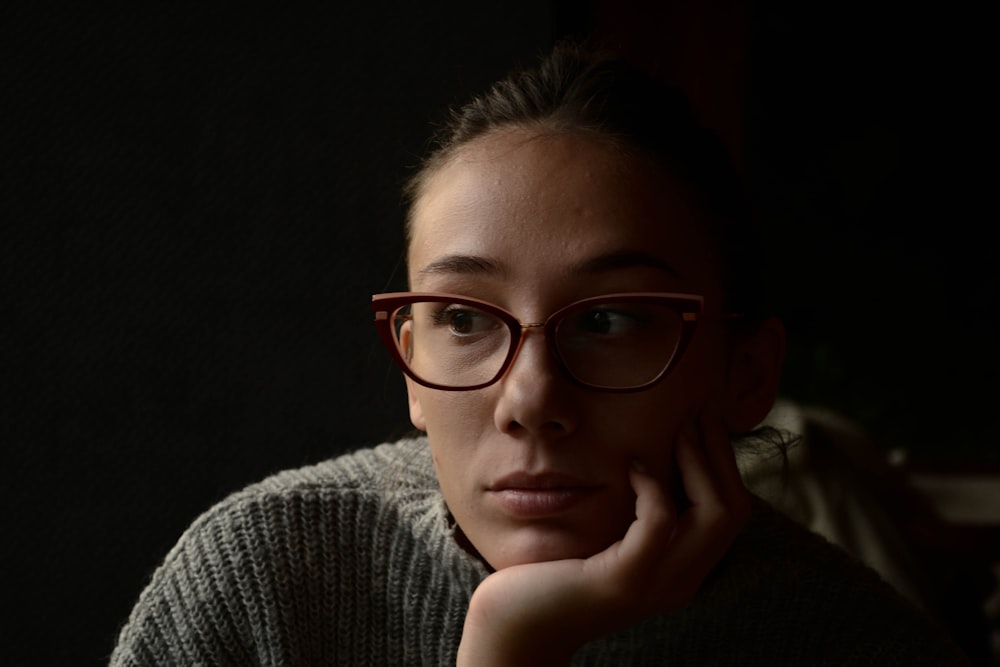 a woman wearing glasses sitting in a dark room