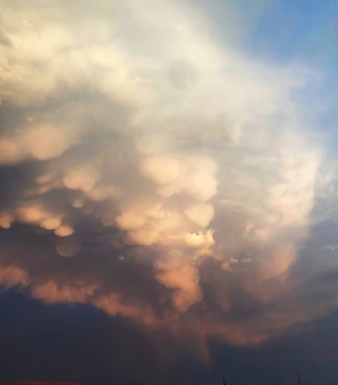 Large, billowing clouds dominate the sky, featuring a mix of soft, rounded shapes with a gentle glow. The cloud formation displays various shades blending from light to darker hues, creating a dynamic and textured appearance.