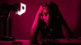 A young candidate sitting at a desk, looking stressed while reviewing notes under soft blue lighting.