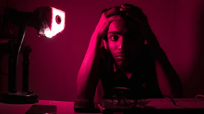 A young candidate sitting at a desk, looking stressed while reviewing notes under soft blue lighting.