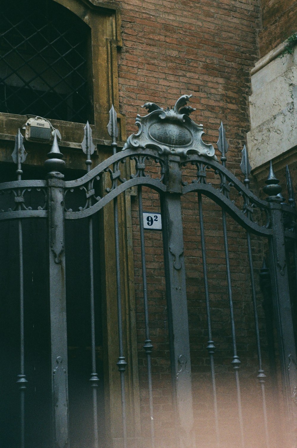 an iron gate with a clock on it in front of a brick building