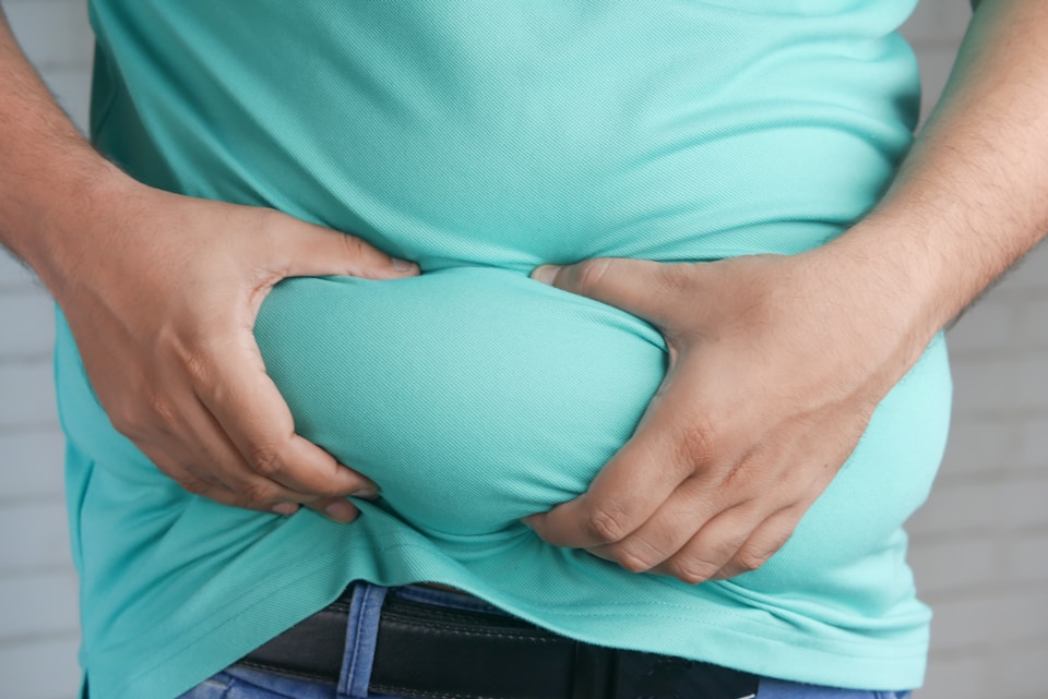 Man in a green shirt pinching his side, representing a focus on weight loss goals