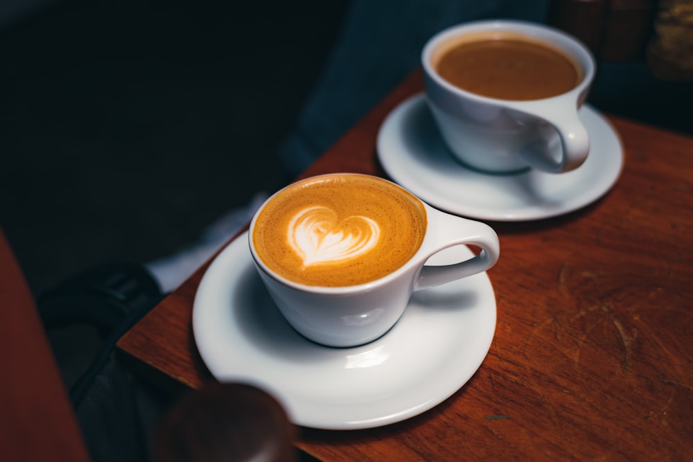 two cups of coffee sitting on top of a wooden table