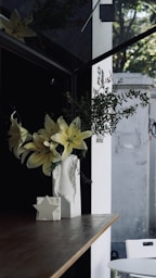 a white vase with yellow flowers on a table