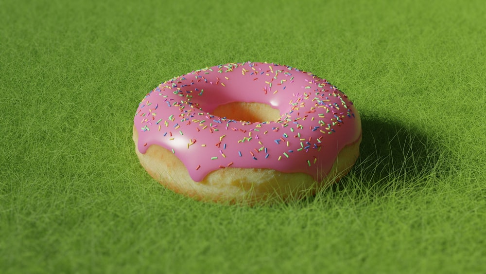a pink donut with sprinkles on a green surface