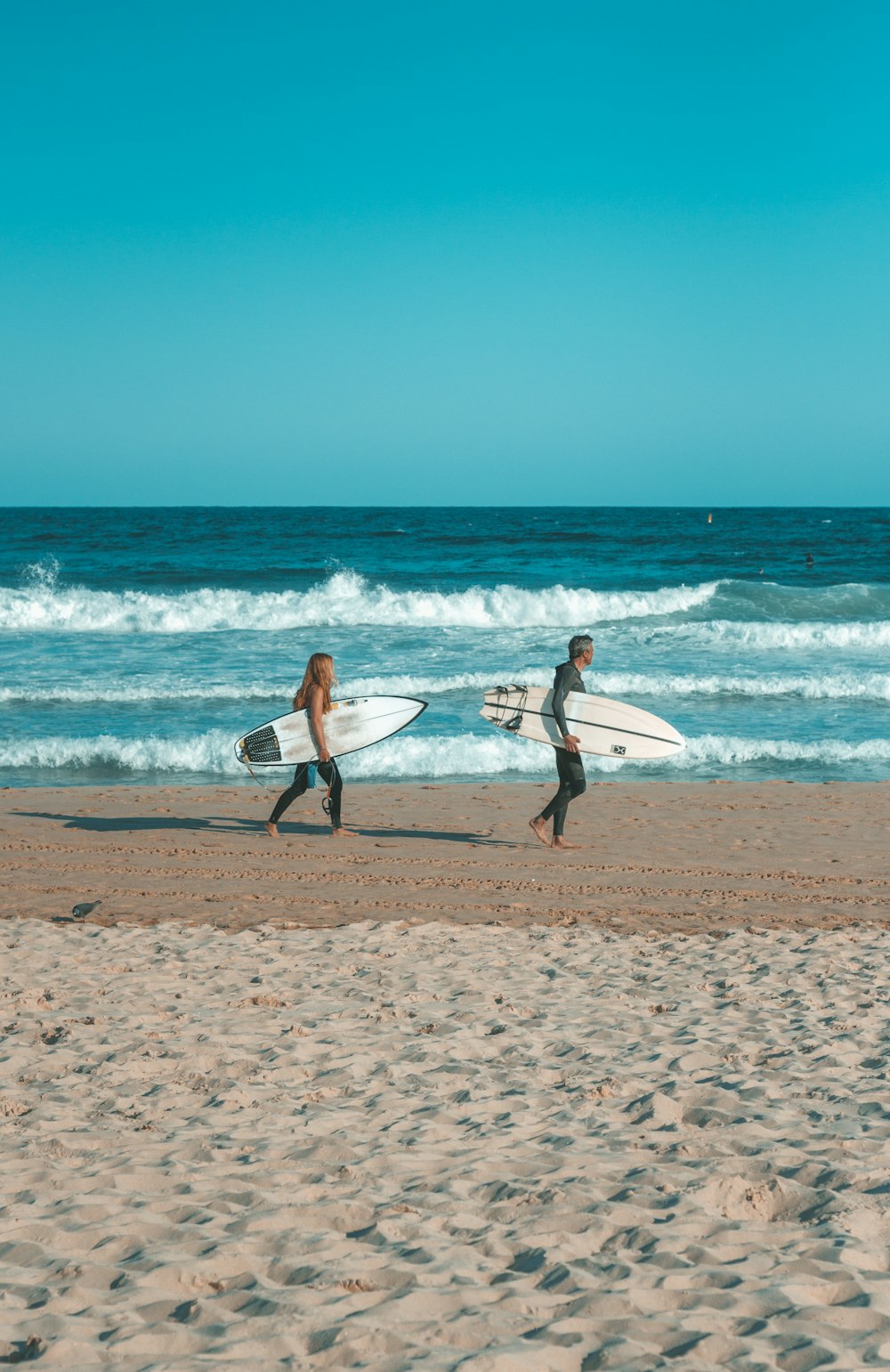 duas pessoas andando na praia com pranchas de surf