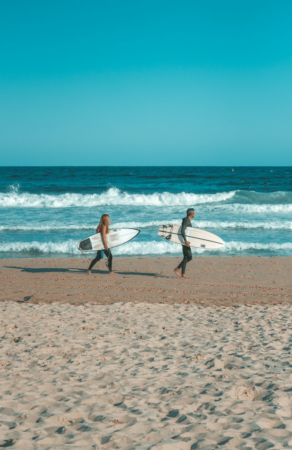 two people walking on the beach with surfboards