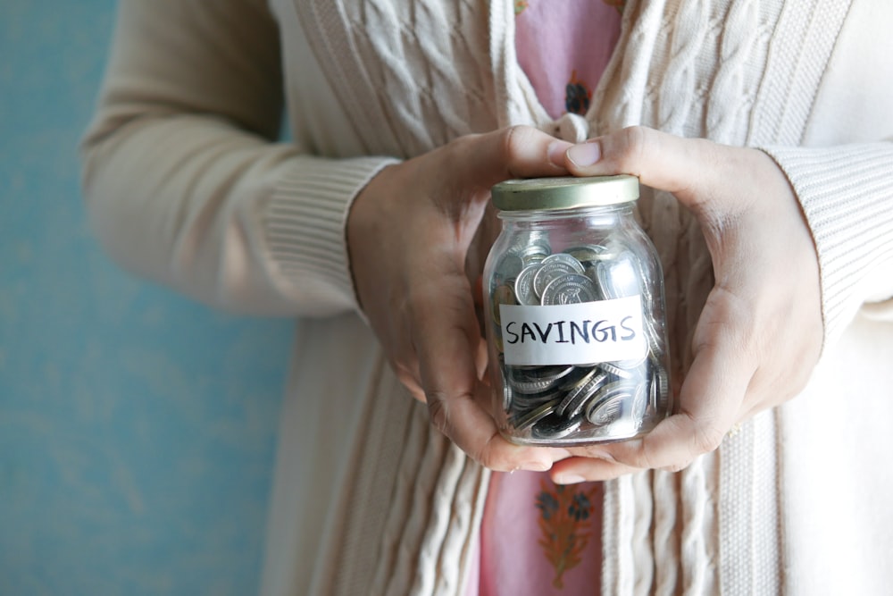 a woman holding a jar with savings written on it