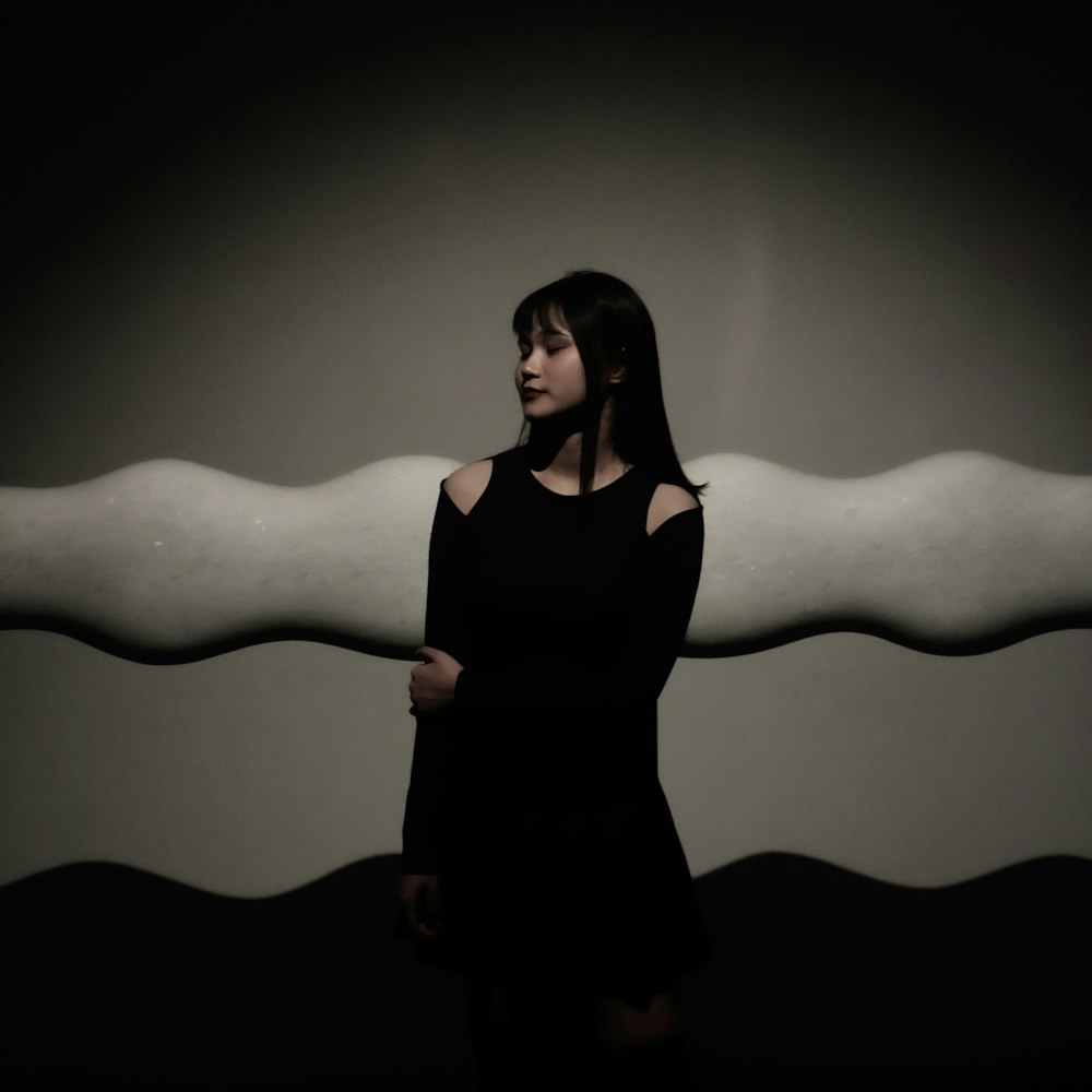 a woman in a black dress standing in front of a white object
