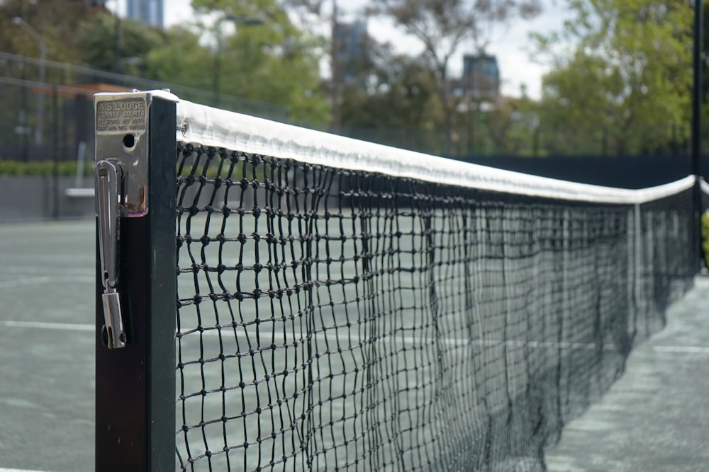 a tennis court with a black net and trees in the background