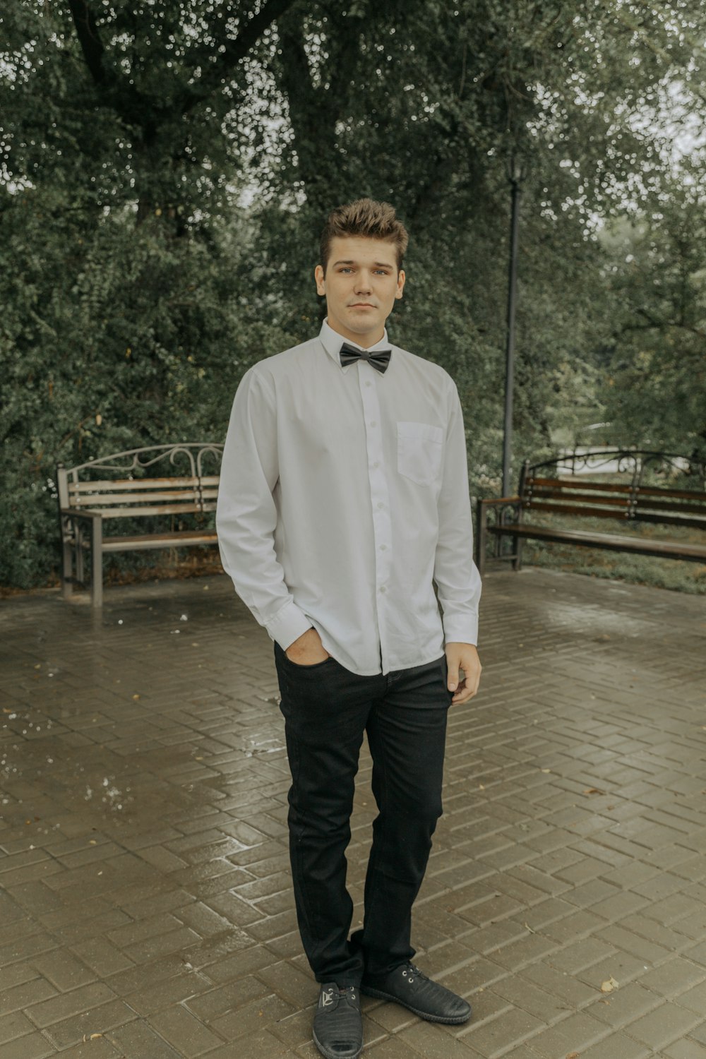 a young man wearing a bow tie standing in a park