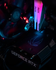The image features the interior of a computer with a focus on a graphics card labeled 'GEFORCE RTX' and RGB lighting components. The lighting displays vibrant hues of pink, blue, and red, illuminating the surrounding hardware.
