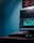 A computer monitor displays video editing software with a timeline and various clips. The setup includes a keyboard and a mouse, situated on a desk in a room with a bluish hue.