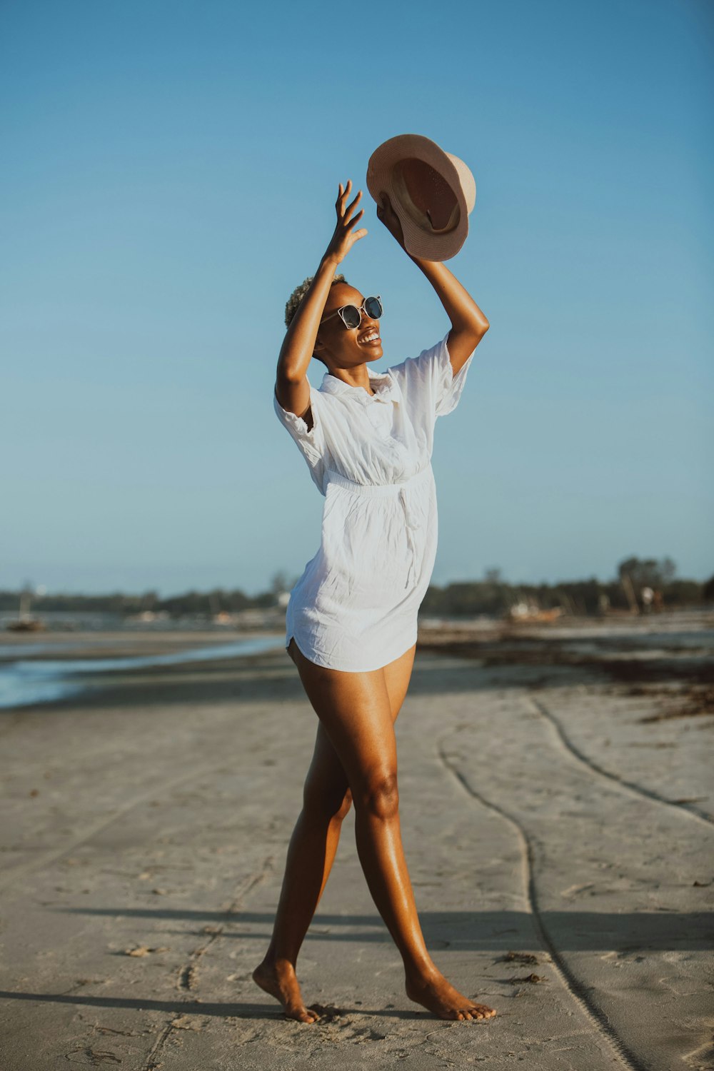 a woman in a white dress and hat on the beach