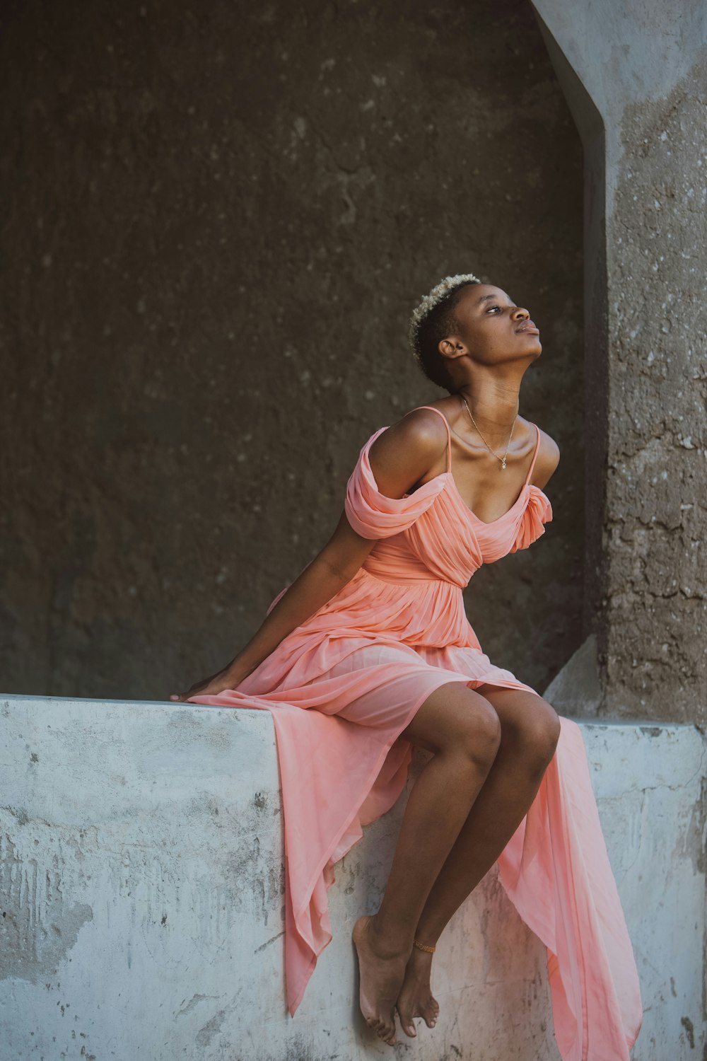 a woman in a pink dress sitting on a ledge