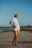 A confident woman in an elegant Coraluz resort dress walking along a sandy shore.