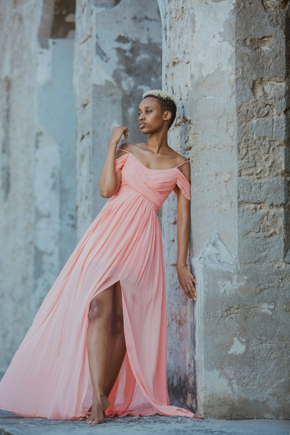 a woman in a pink dress leaning against a wall