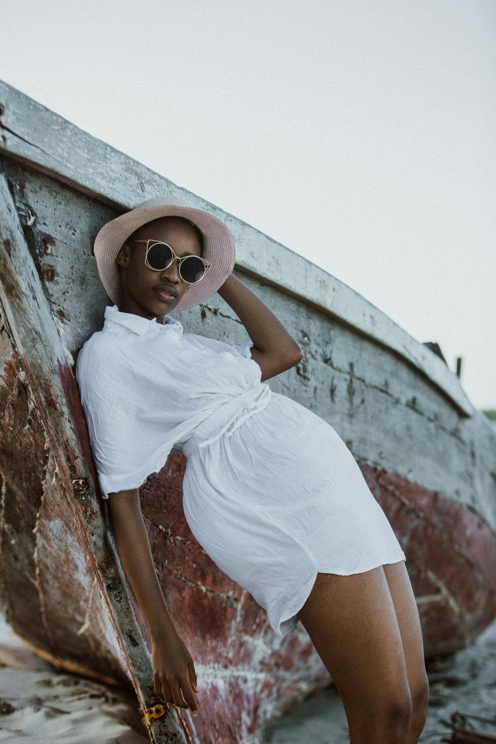 a woman in a white dress and hat leaning against a boat