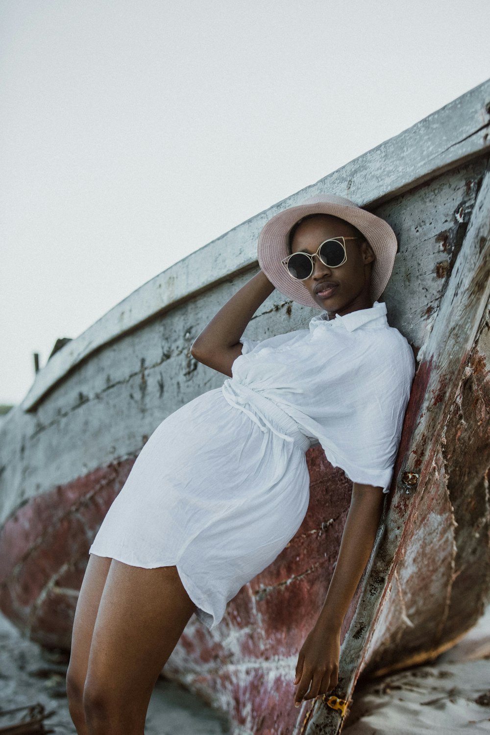 a woman in a hat and sunglasses leaning against a boat