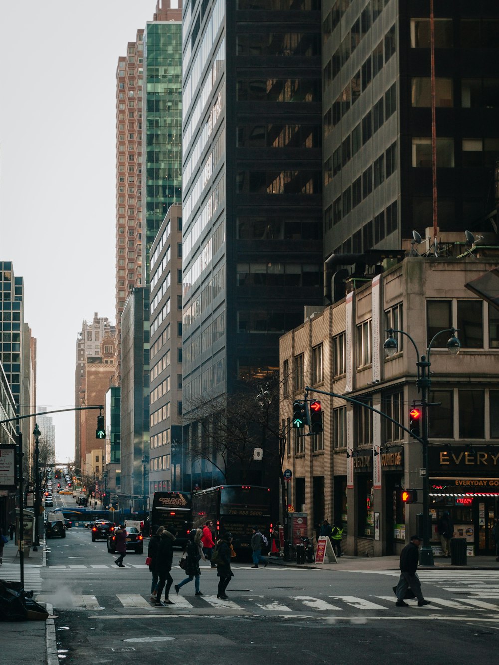 a group of people walking across a street next to tall buildings