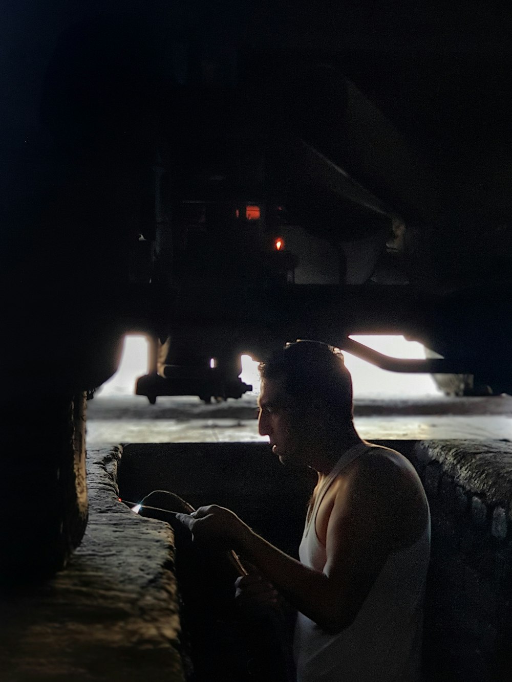 um homem em uma camiseta do tanque sentado sob um caminhão