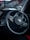 A close-up view of a car steering wheel featuring the Kia logo in the center. The dashboard and part of the interior, with some controls and dials visible, are shown in low light. The background appears blurred, hinting at a street or outdoor setting.