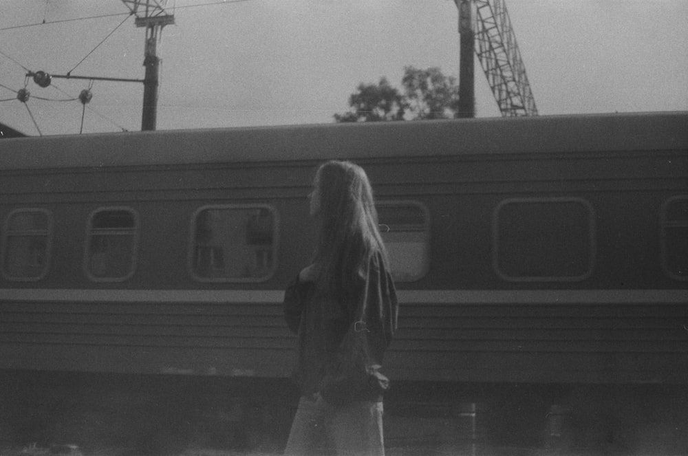 a black and white photo of a woman standing in front of a train